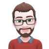 Person with glasses, brown beard, and brown hair in a sweater and collared shirt